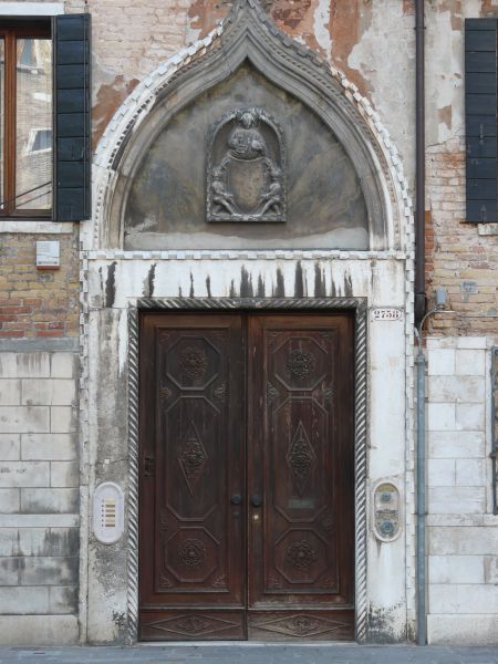 Worn dark brown wooden door with intricately-designed trim and dome-shaped crown.